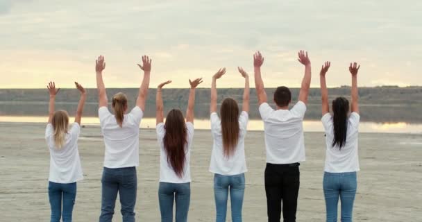 Team van vrienden golven opgeheven handen op vlakke rivieroever — Stockvideo