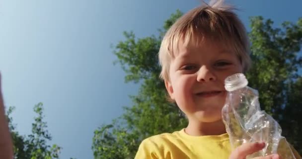 Çocuk, gülümseyerek plastik şişeleri çöp poşetine dolduruyor. — Stok video