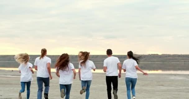Група друзів біжить і піднімає руки на твердому березі річки — стокове відео