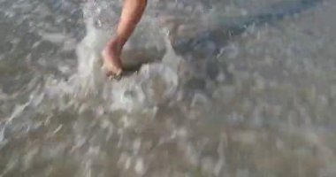 Küçük kız kumsalda koşar köpüklü dalgalarla yıkanır