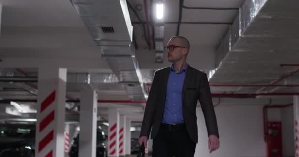 Mannen i kostym går i underjordisk parkering letar efter sin bil — Stockvideo