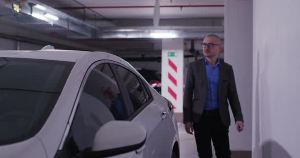 Homem caminha abrindo carro branco em pé no estacionamento subterrâneo — Vídeo de Stock