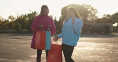 Kız arkadaşlar alışverişe bakar ve gün batımına karşı sarılırlar.