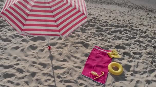 Velký pruhovaný deštník instalovaný v písku a plážových nezbytnostech — Stock video