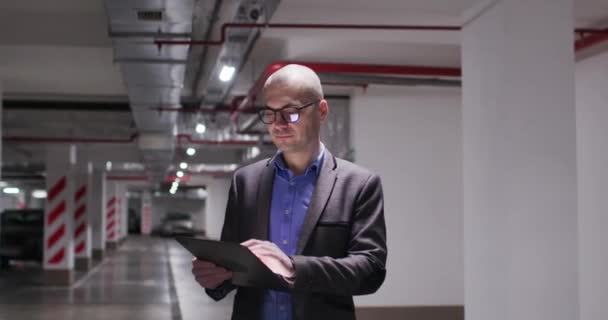 Empresário verifica relatórios em tablet de pé no estacionamento — Vídeo de Stock