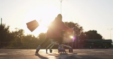 Kadın arkadaşıyla alışveriş arabasında paten kayıyor.