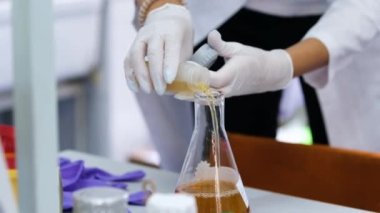 Bilim adamı laboratuardaki cam şişeye kahverengi reaktör döküyor.