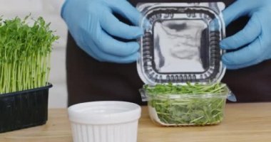 Kadın plastik kutudan bezelye filizlerini çıkarıp kaseye koyuyor.