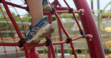 Mavi ayakkabılı küçük bir çocuğun oyun parkında ip ağdan aşağı inmesi. Aktif anaokulu öğrencisi çocuk parkına tırmanma oyunu oynuyor.