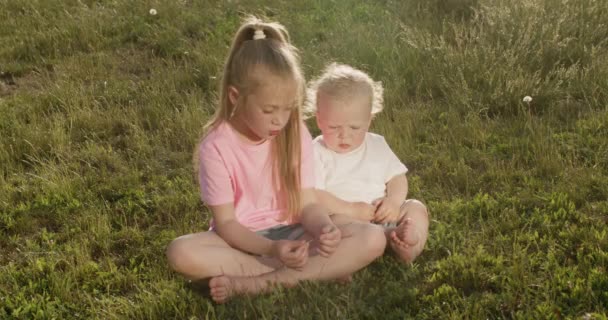 Elementary School Girl Sits Meadow Little Brother Plays Grass Little — Vídeo de Stock