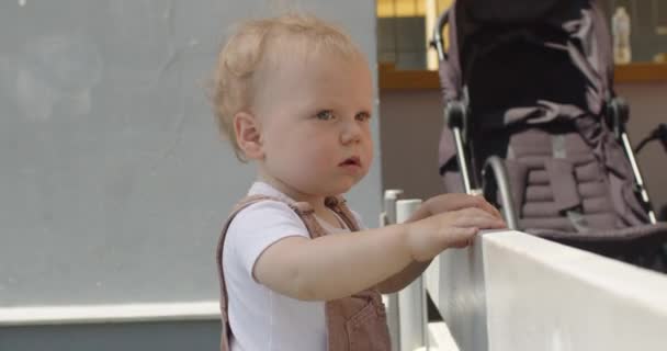Cute Blond Toddler Boy Stands Grey Wall Holding Fence Hands — Αρχείο Βίντεο