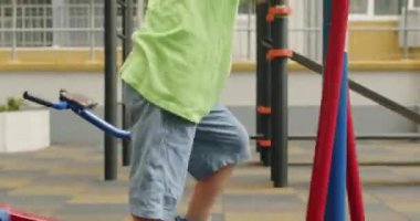 Preschooler boy enjoys doing exercise on bicycle machine on playground. Excited child plays alone on playground on gloomy morning smiling closeup