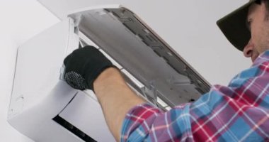 Technician removes dirty air filter from conditioner and carefully examines detail. Repairman wearing black gloves shows appliance without system cleaning