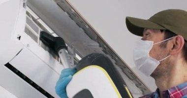 Beyaz tıbbi maske takan adam farklı parçacıkların klima hava filtrelerini vakumluyor. Tamirci, klimayı tıkanan toz ve kabartıcıdan temizliyor.