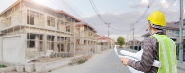 İnşaat şantiyesindeki koruyucu miğfer ve planlar üzerinde çalışan genç profesyonel mühendis.