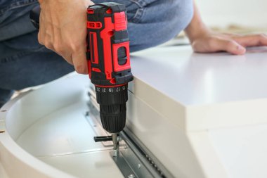 Beyaz masa mobilyalarını kablosuz tornavida kullanarak evde monte eden adam.