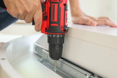 Beyaz masa mobilyalarını kablosuz tornavida kullanarak evde monte eden adam.