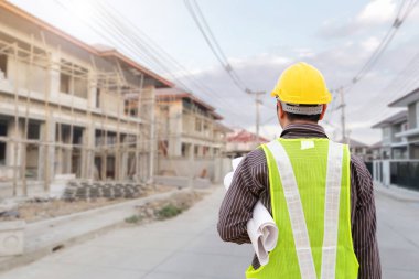 İnşaat şantiyesindeki koruyucu miğfer ve planlar üzerinde çalışan genç profesyonel mühendis.