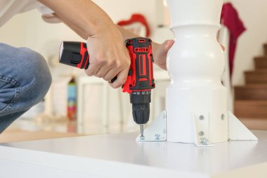 Beyaz masa mobilyalarını kablosuz tornavida kullanarak evde monte eden adam.