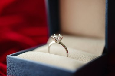 Kırmızı kumaş arka planda mücevher hediye kutusunda elmas yüzük.