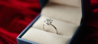 Kırmızı kumaş arka planda mücevher hediye kutusunda elmas yüzük.