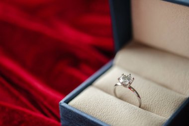 Kırmızı kumaş arka planda mücevher hediye kutusunda elmas yüzük.