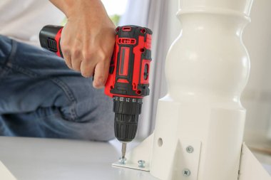 Beyaz masa mobilyalarını kablosuz tornavida kullanarak evde monte eden adam.