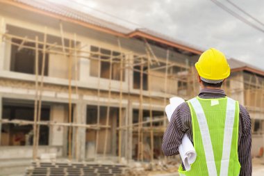 İnşaat şantiyesindeki koruyucu miğfer ve planlar üzerinde çalışan genç profesyonel mühendis.