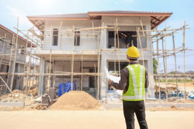 İnşaat şantiyesindeki koruyucu miğfer ve planlar üzerinde çalışan genç profesyonel mühendis.