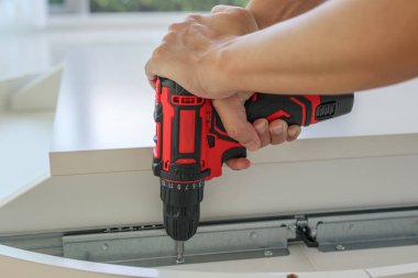 Beyaz masa mobilyalarını kablosuz tornavida kullanarak evde monte eden adam.