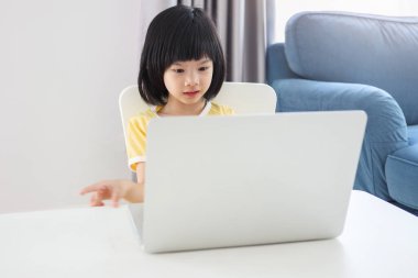 Küçük Asyalı kız öğrenci çevrimiçi evde dizüstü bilgisayar kullanıyor.