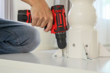 Beyaz masa mobilyalarını kablosuz tornavida kullanarak evde monte eden adam.