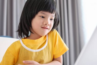 Küçük Asyalı kız öğrenci çevrimiçi evde dizüstü bilgisayar kullanıyor.