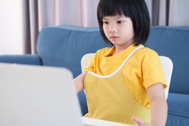 Küçük Asyalı kız öğrenci çevrimiçi evde dizüstü bilgisayar kullanıyor.