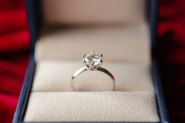 Kırmızı kumaş arka planda mücevher hediye kutusunda elmas yüzük.