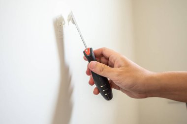 Çatlak beyaz duvarı spatulayla tamir eden adam.