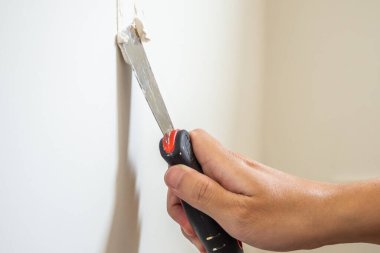 Çatlak beyaz duvarı spatulayla tamir eden adam.