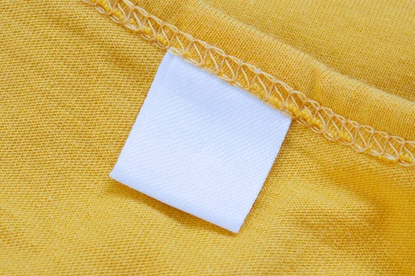 Yeni sarı gömlek arka planında beyaz boş giyim etiketi