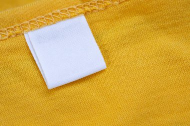 Yeni sarı gömlek arka planında beyaz boş giyim etiketi