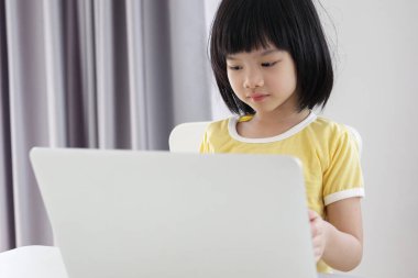 Küçük Asyalı kız öğrenci çevrimiçi evde dizüstü bilgisayar kullanıyor.