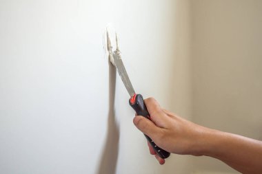 Çatlak beyaz duvarı spatulayla tamir eden adam.