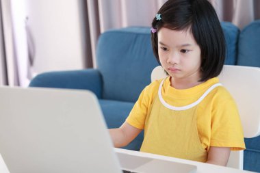 Küçük Asyalı kız öğrenci çevrimiçi evde dizüstü bilgisayar kullanıyor.