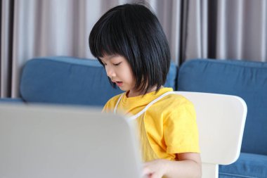 Küçük Asyalı kız öğrenci çevrimiçi evde dizüstü bilgisayar kullanıyor.