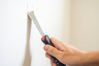Çatlak beyaz duvarı spatulayla tamir eden adam.