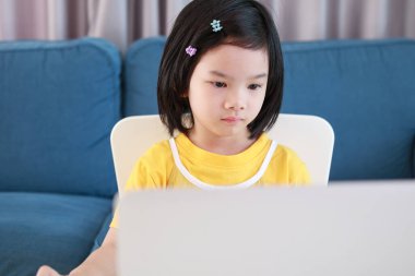 Küçük Asyalı kız öğrenci çevrimiçi evde dizüstü bilgisayar kullanıyor.