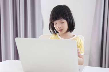 Küçük Asyalı kız öğrenci çevrimiçi evde dizüstü bilgisayar kullanıyor.