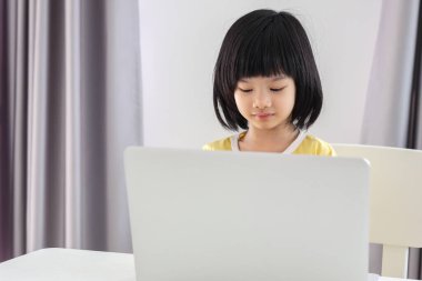 Küçük Asyalı kız öğrenci çevrimiçi evde dizüstü bilgisayar kullanıyor.