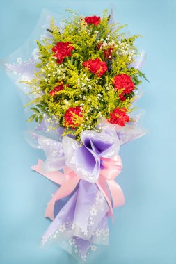 flower bouquet of red carnation with green leaves on blue background