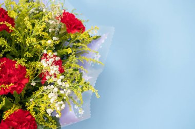 flower bouquet of red carnation with green leaves on blue background