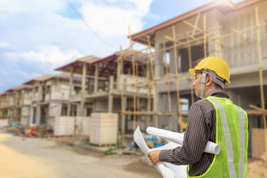 İnşaat şantiyesindeki koruyucu miğfer ve planlar üzerinde çalışan genç profesyonel mühendis.